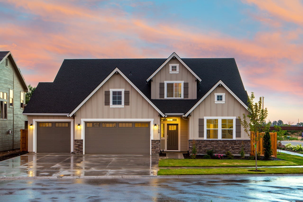 Modern residential home with a welcoming entrance, featuring a combination of beige siding and stone accents, two garage doors, and landscaped yard, reflecting real estate opportunities in Rochester Hills.