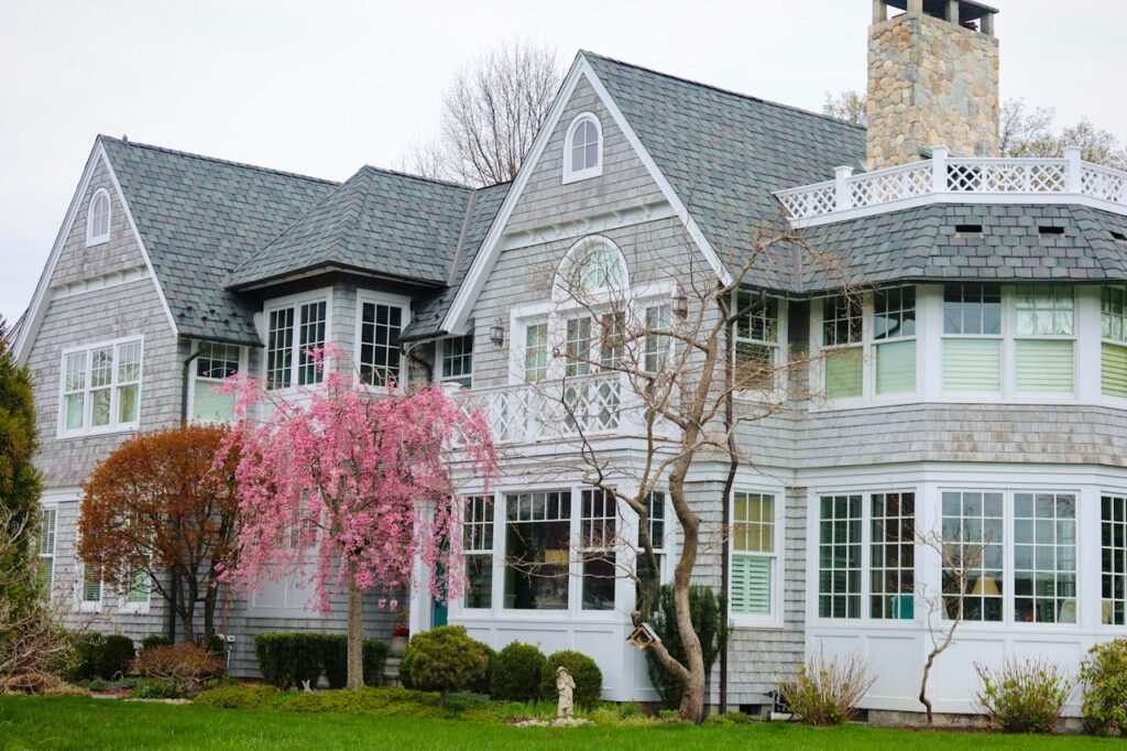 Charming residential property featuring a shingle-style exterior, large windows, and a blooming pink tree, representing ValCrest Properties' real estate offerings in Troy, Michigan.