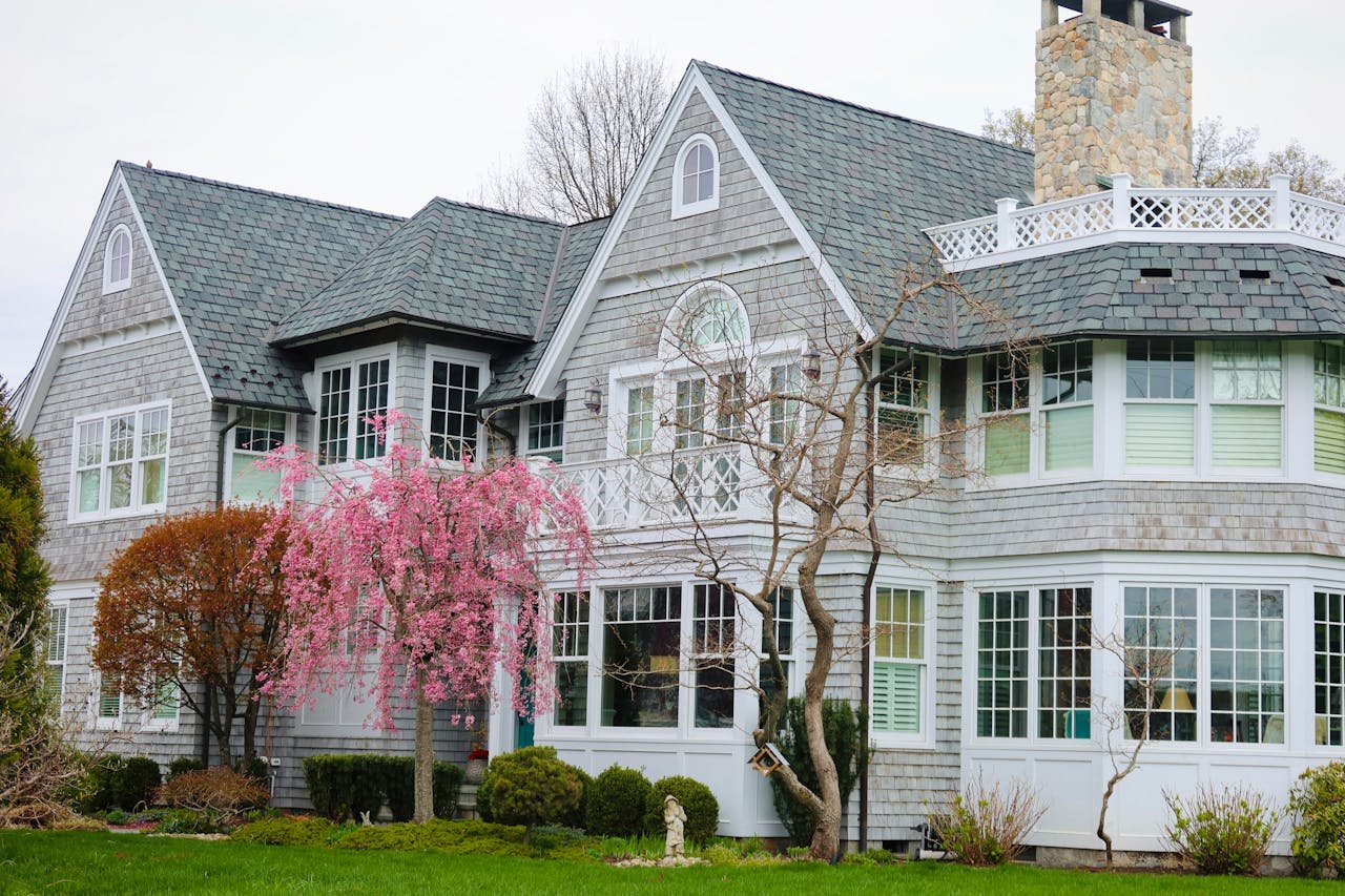 Charming residential property with a gray shingle exterior, large windows, and a blooming pink cherry tree, representing ValCrest Properties' focus on real estate in Rochester Hills.